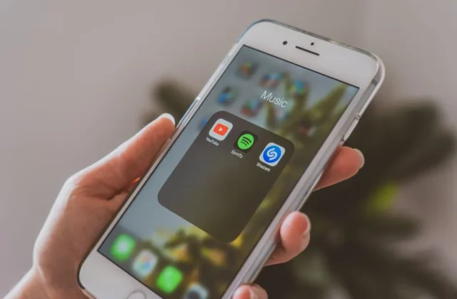 Hand holding a smartphone displaying popular music apps like Spotify and Shazam in a close-up shot.