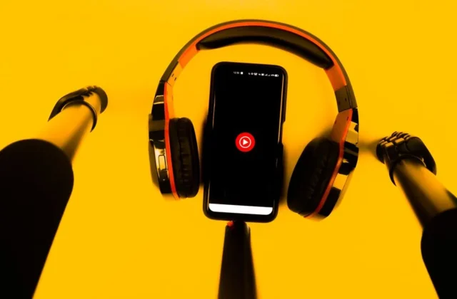 A smartphone with wireless headphones and microphone set against a vibrant yellow background.
