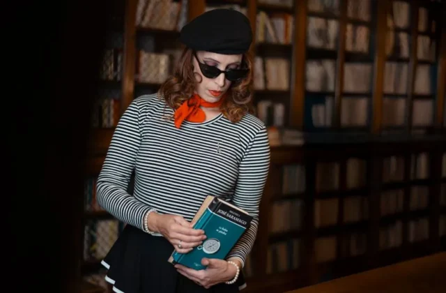 Elegant woman in a striped shirt and beret reading in a classic library setting.