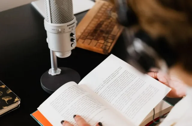 Close-up of a person reading with a microphone on a desk.