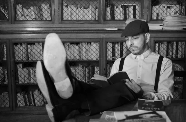 Black and white photo of a man reading in a vintage library setting.