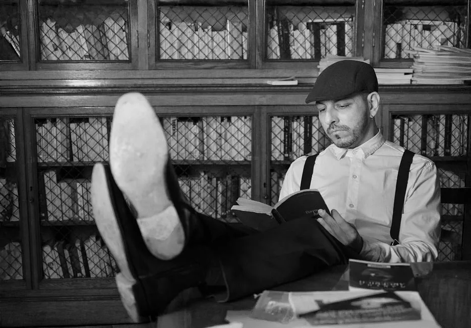 Black and white photo of a man reading in a vintage library setting.
