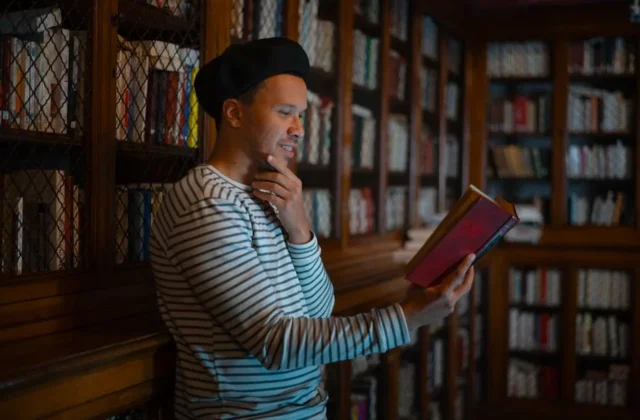A man enjoys reading in a cozy library with wooden bookshelves, creating a reflective ambiance.