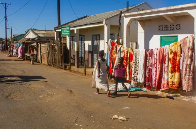 Two children walk past colorful textiles in sunny Ankililoaka, Madagascar.